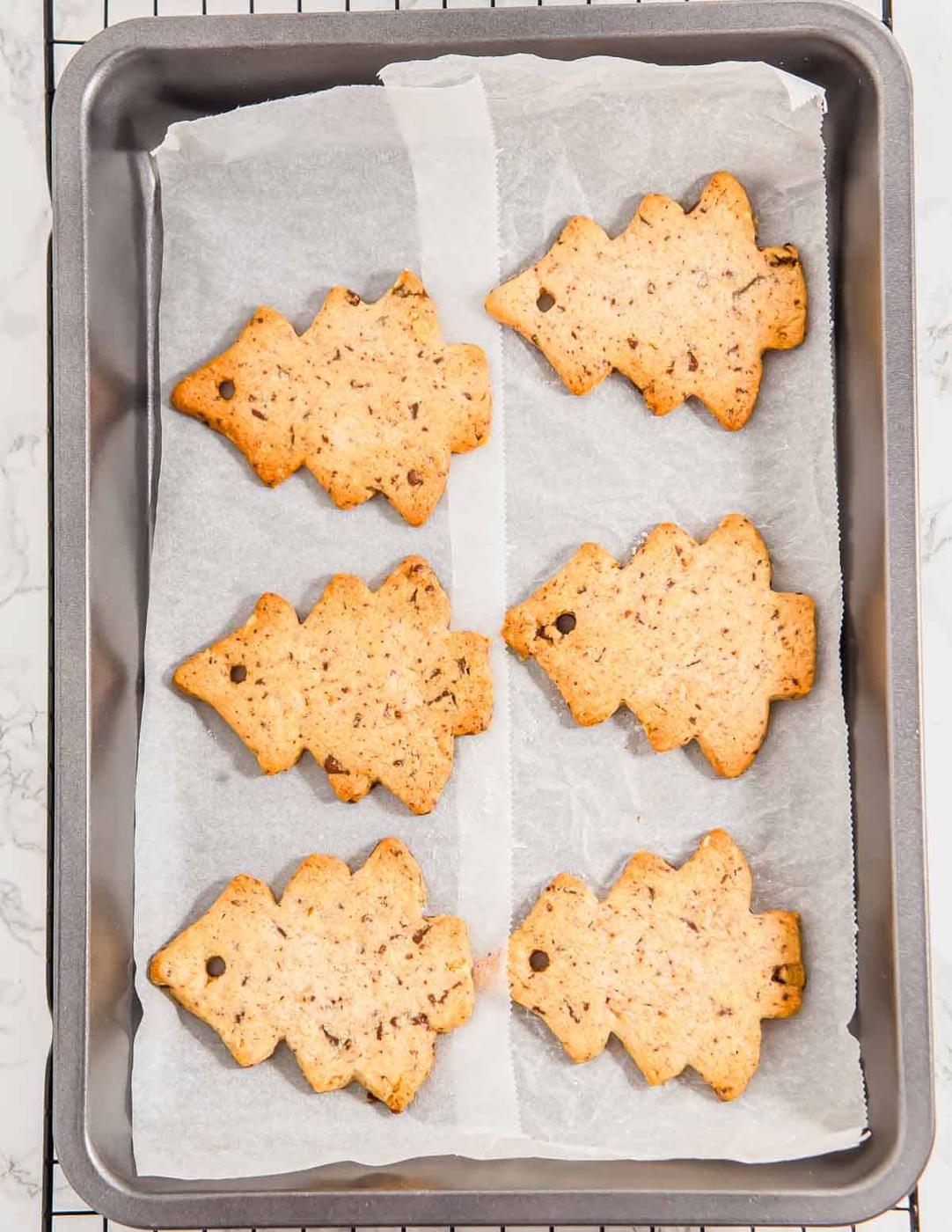 Baked Christmas tree cookies on parchment paper on top of a baking sheet and cooling rack.