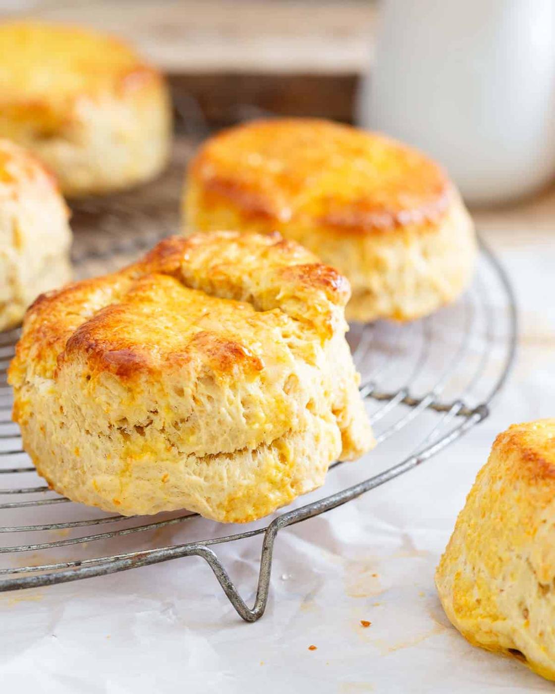 Golden-brown honey biscuits cooling on a wire rack, with a focus on one prominently in the foreground, surrounded by parchment paper.