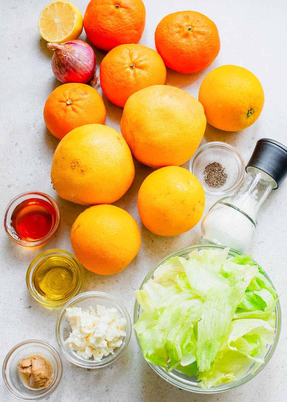 Citrus laying on a counter top and a bowl of lettuce with other ingredients for a salad dressing.
