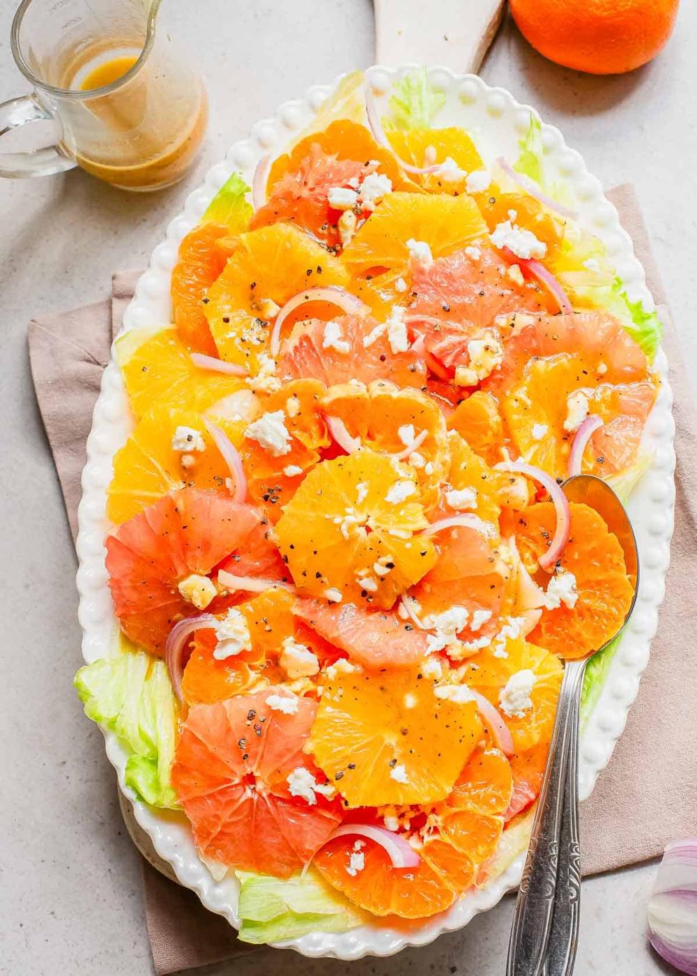Orange, grapefruit and mandarin salad on a white plate with a spoon.