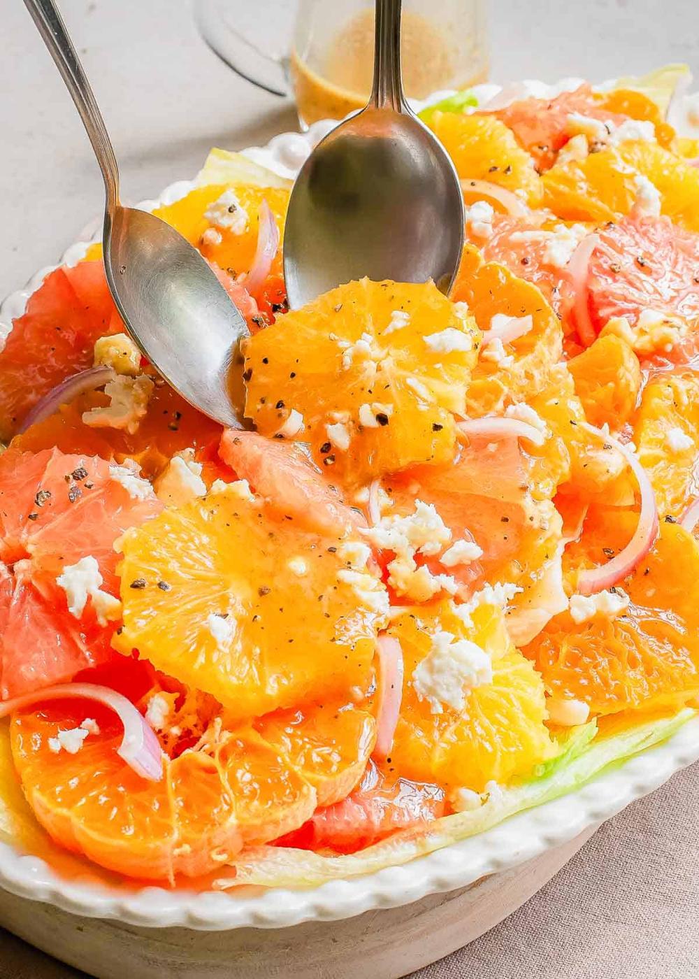 A serving plate with citrus salad and two serving spoons.