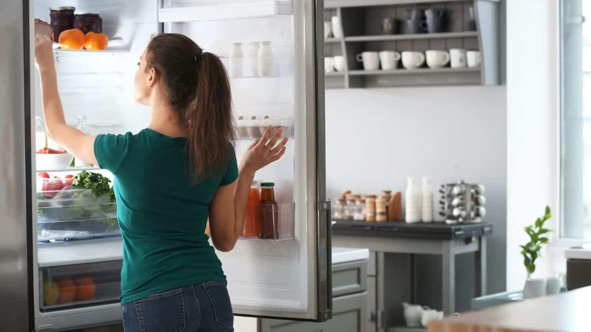 A woman opening the door of a refrigerator.