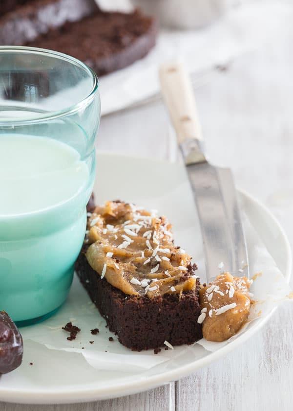 Date spread on a piece of chocolate bread next to a glass of milk.