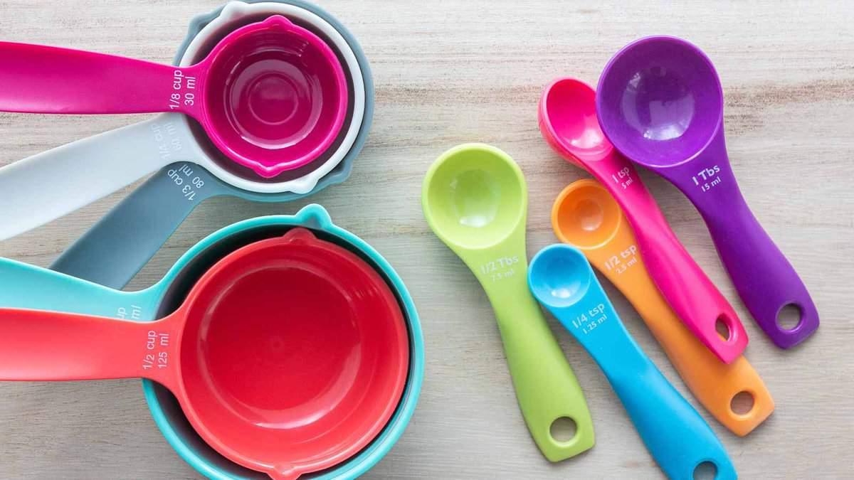 A set of colorful measuring cups and spoons arranged on a wooden surface. The cups and spoons range in size and are vibrant in colors such as pink, orange, green, blue, and purple.