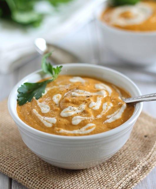 Creamy dairy free tomato soup in a white bowl with spoon garnished with parsley.