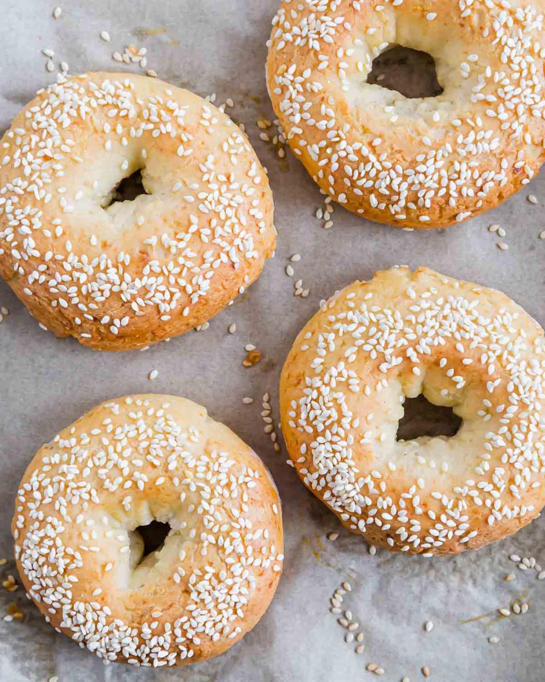 Four sesame seed high protein bagels on parchment paper, viewed from above.