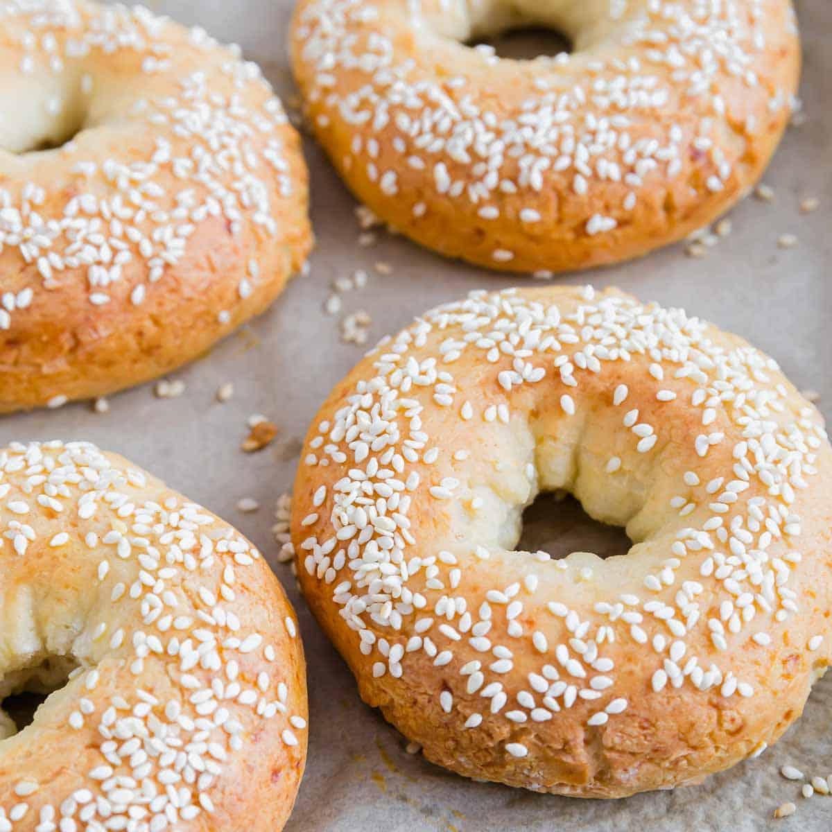 Four sesame seed-topped cottage cheese protein bagels on a parchment-lined surface.