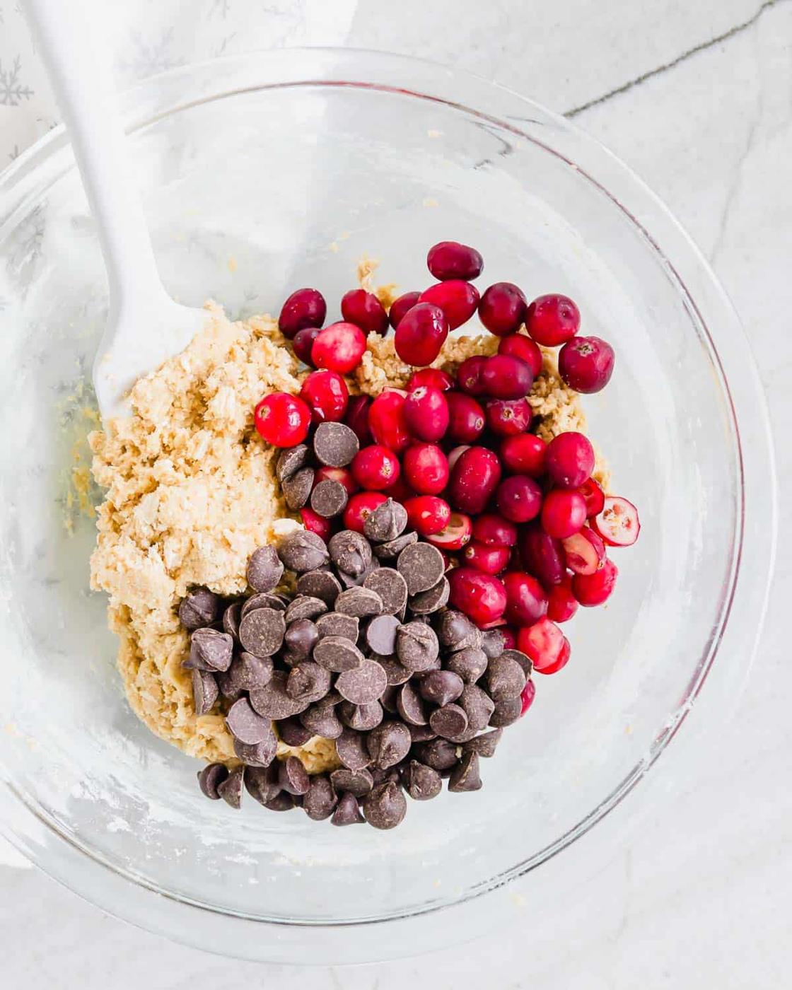 Cranberry chocolate chip cookie dough batter in a glass bowl with a white silicone spatula.