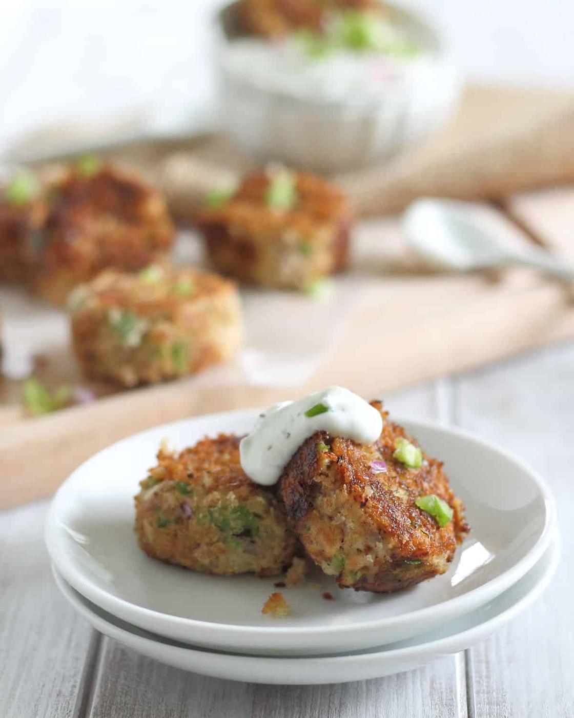 Salmon bites on a white plate with yogurt dill sauce dolloped on top.