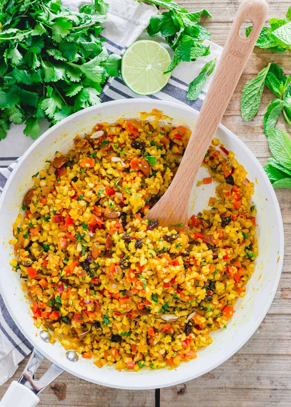 White skillet with curry cauliflower rice and wooden spatula.