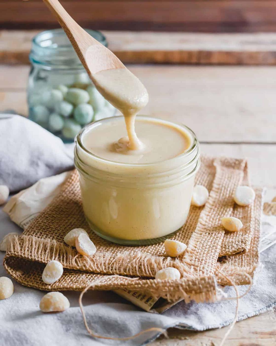 Macadamia nut butter in a glass jar with a wooden spoon.