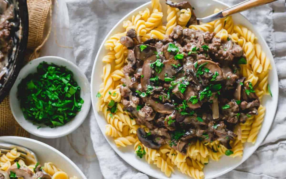 Venison stroganoff on a plate of noodles with mushrooms and parsley.