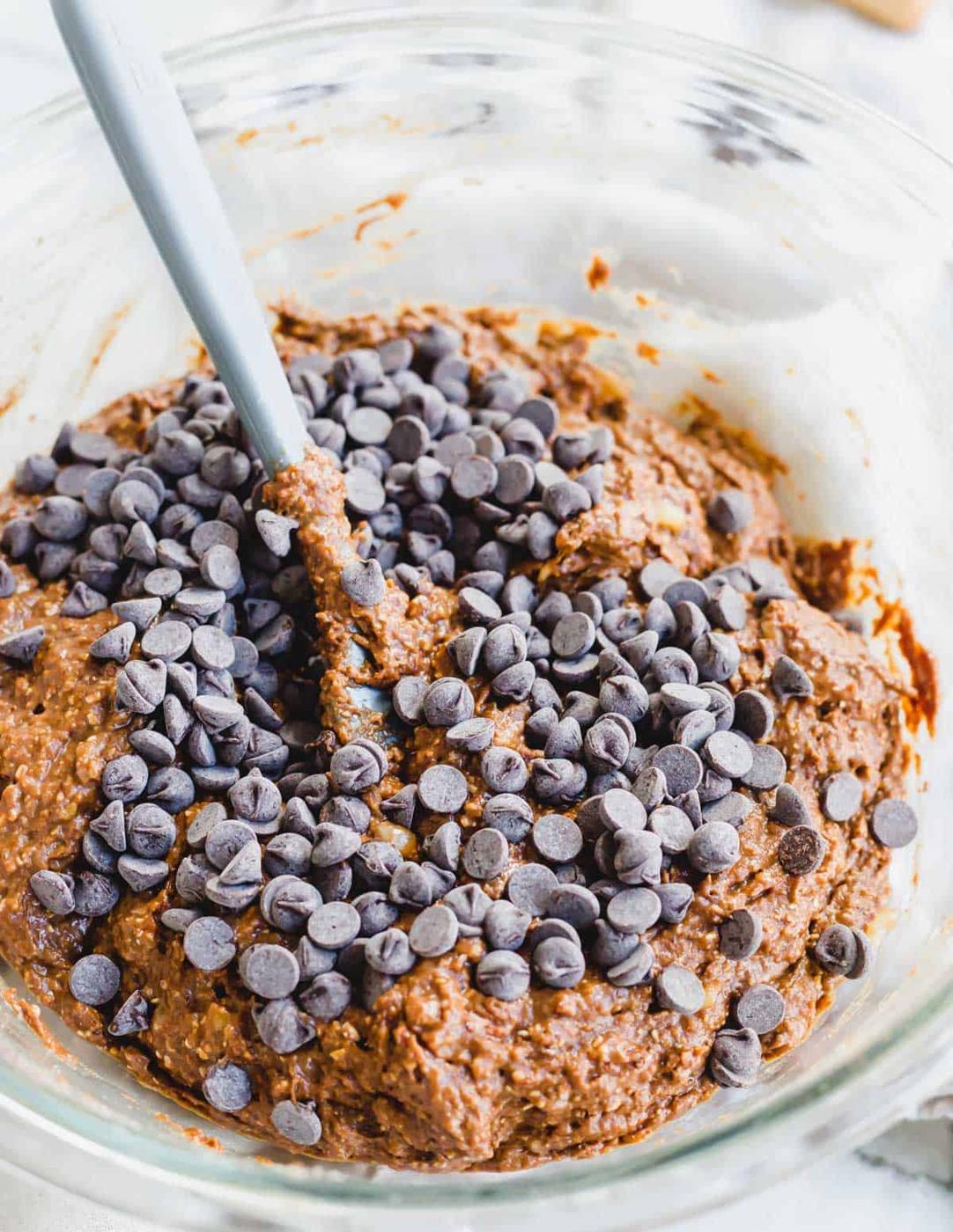 Healthy chocolate banana bread batter in a glass bowl with chocolate chips on top and a spatula.