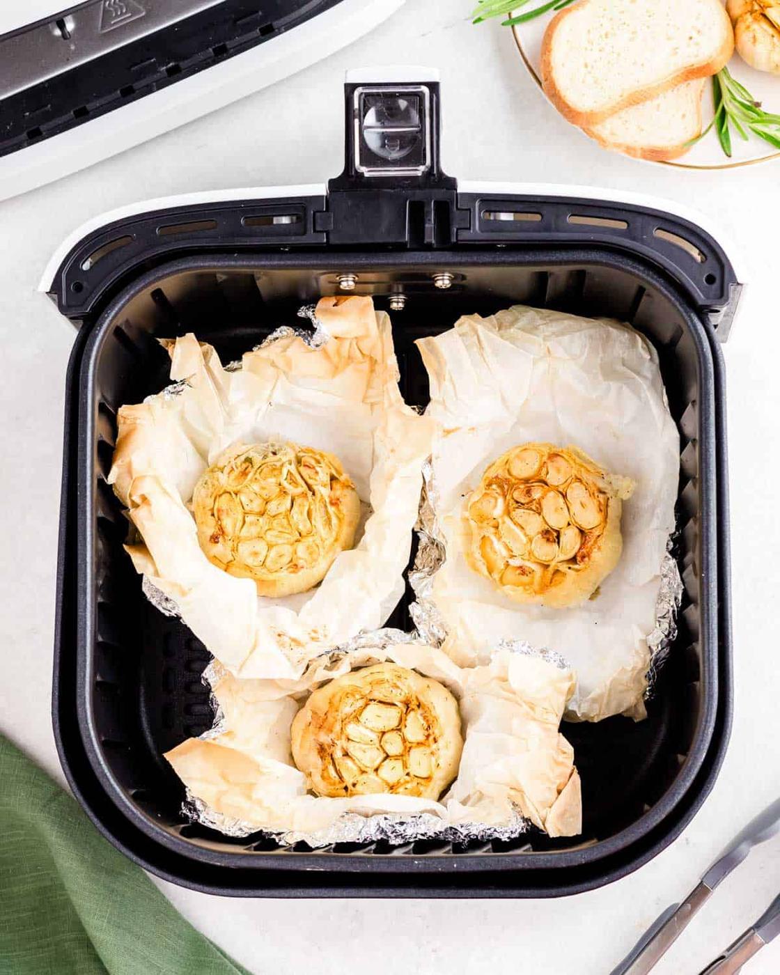 Three heads of garlic wrapped in parchment and aluminum foil in an air fryer.