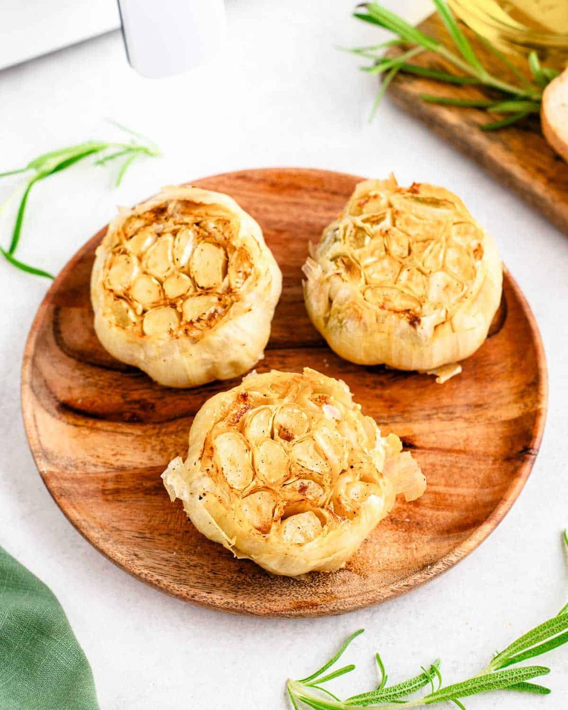 Three air fryer roasted garlic heads on a wooden plate.