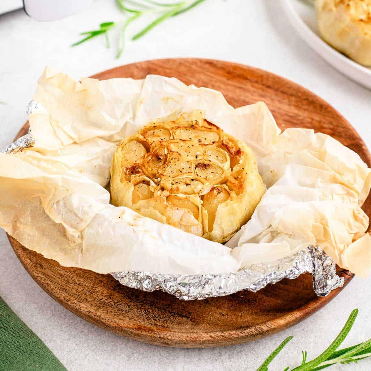 Golden brown head of roasted garlic in parchment paper on a plate.