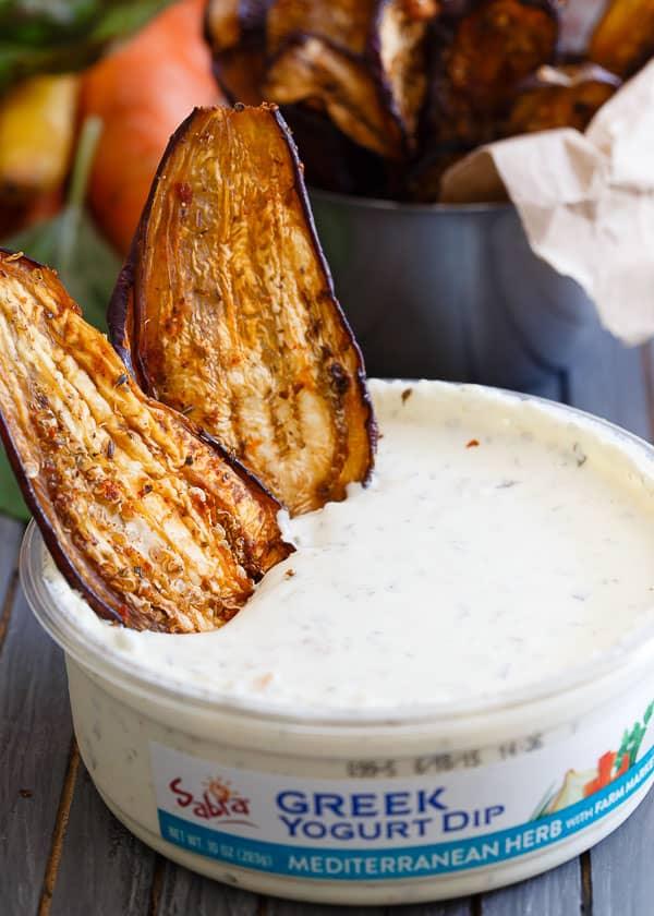 Two eggplant chips standing up in a container of greek yogurt dip.