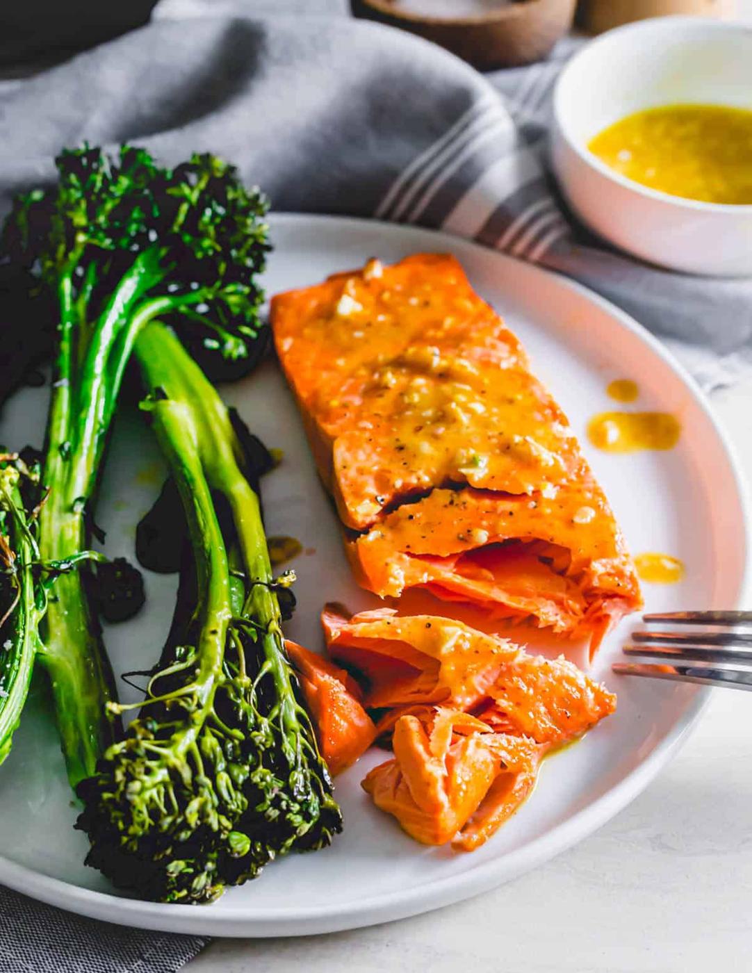 Air fryer frozen salmon on a plate with a fork and broccolini on the side.