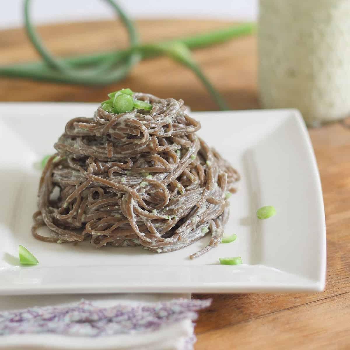 Soba noodles with garlic scape pesto on a white plate.