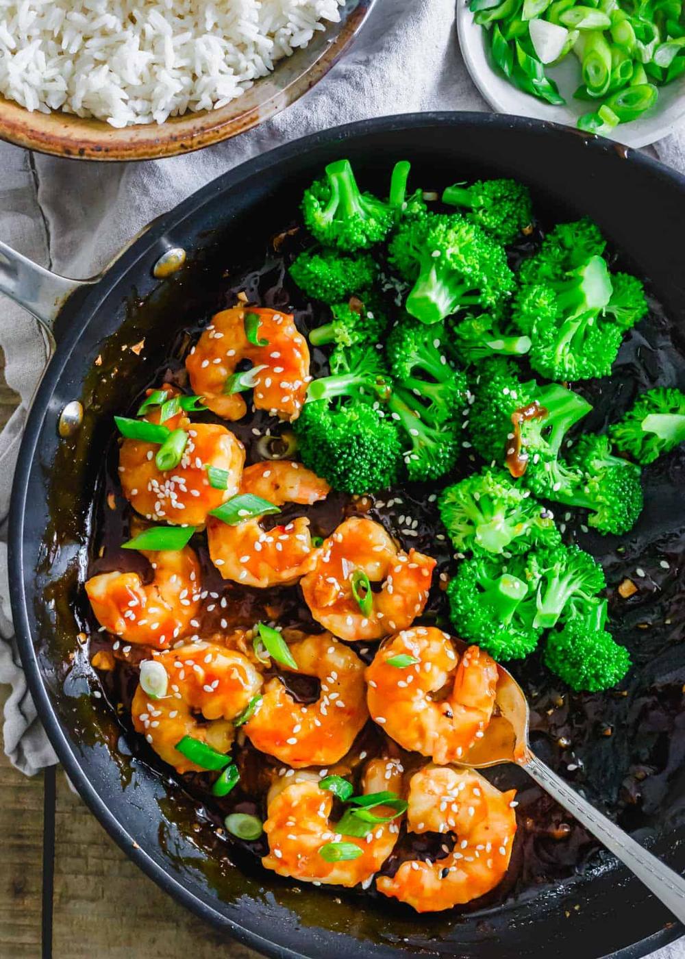 Cooked shrimp coated in General Tso's sauce with broccoli in a skillet.