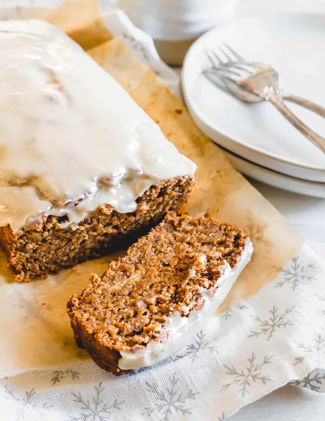 Gingerbread banana bread with molasses and maple tahini glaze sliced on parchment paper.