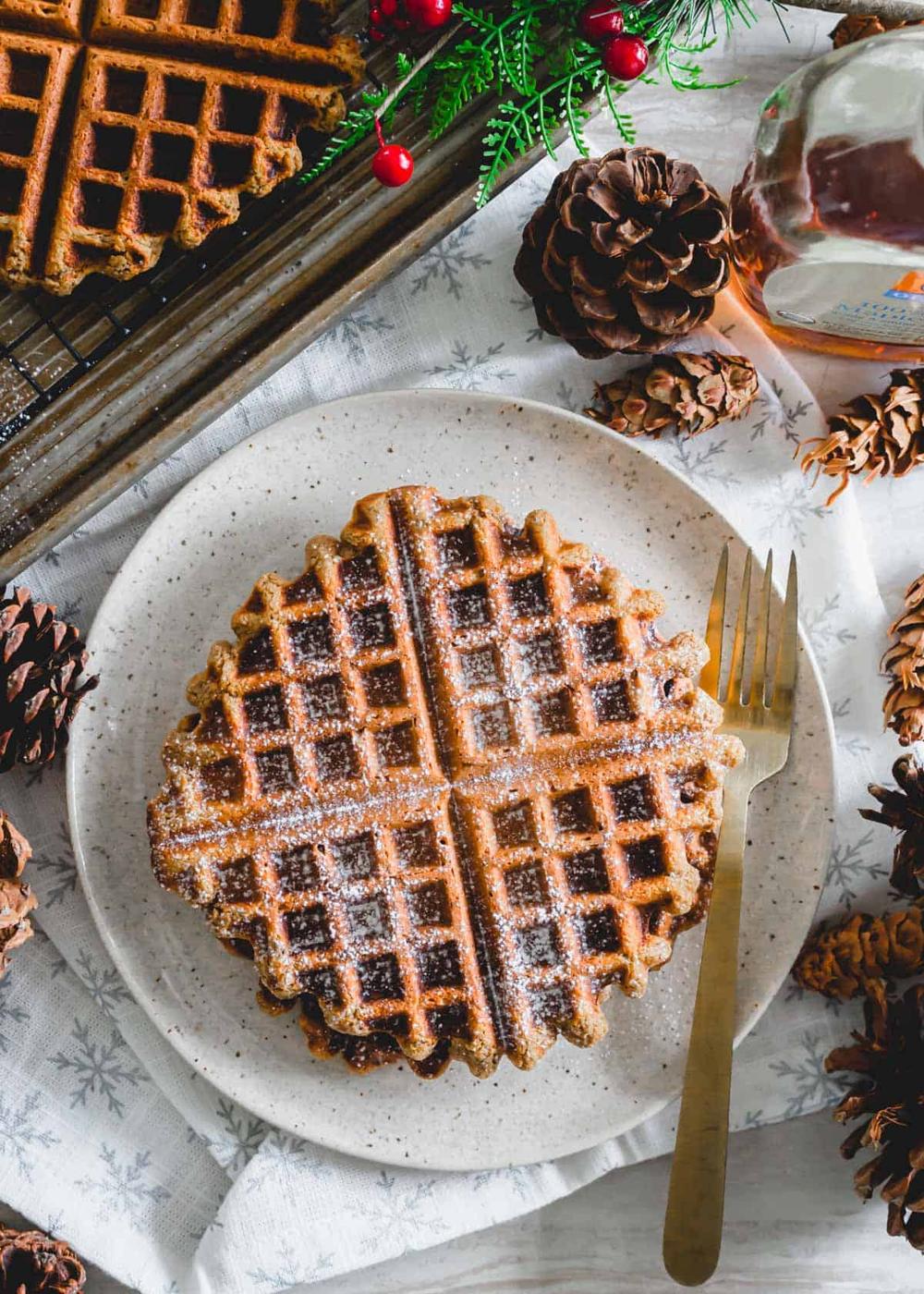 Gingerbread waffles with powdered sugar on a plate with a fork.