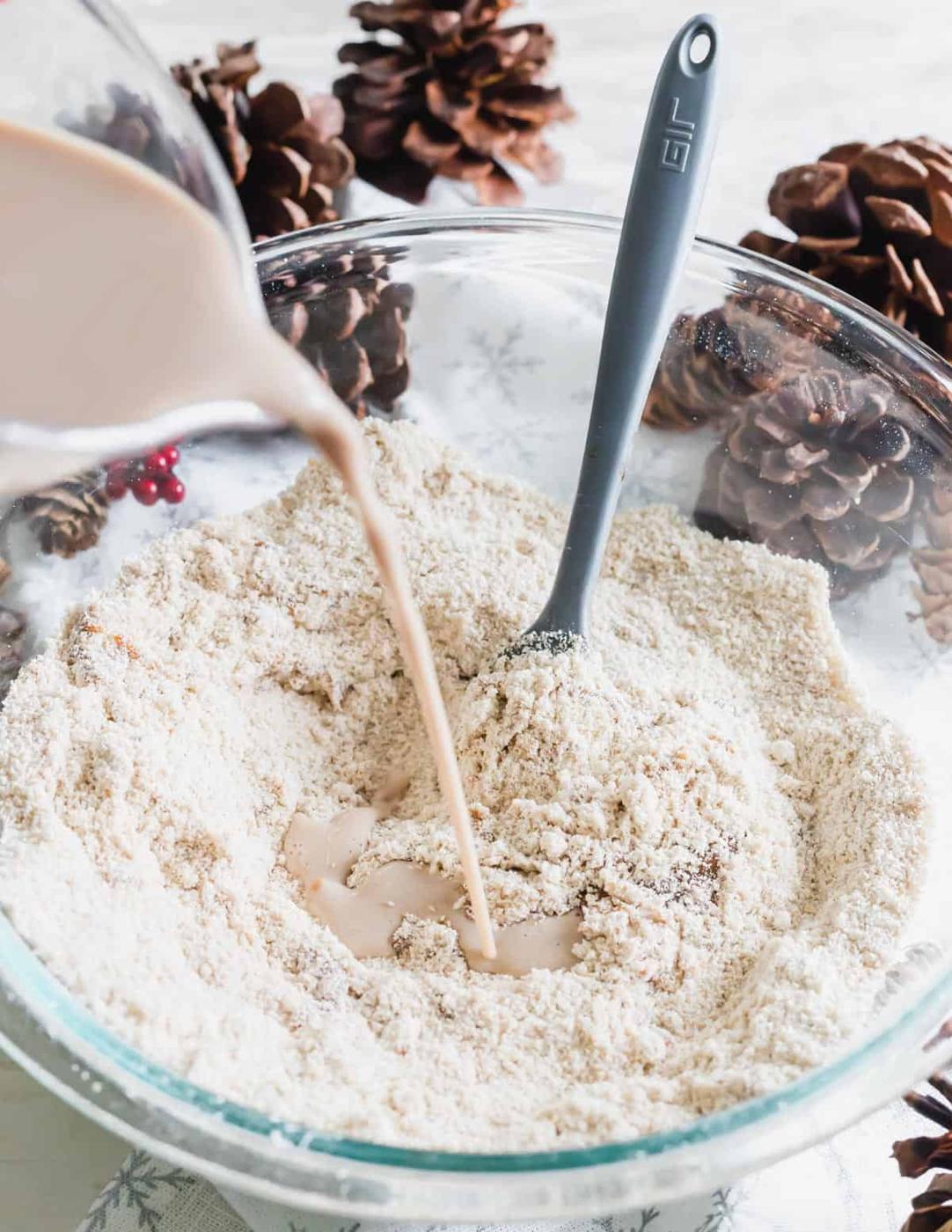 Adding milk to flour in a bowl to make a gingerbread waffle recipe.
