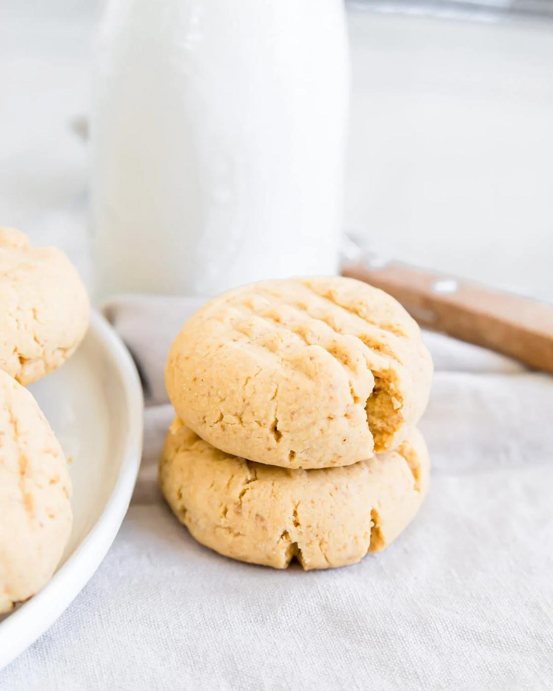 Two gluten-free peanut butter cookies stacked next to a bottle of milk.