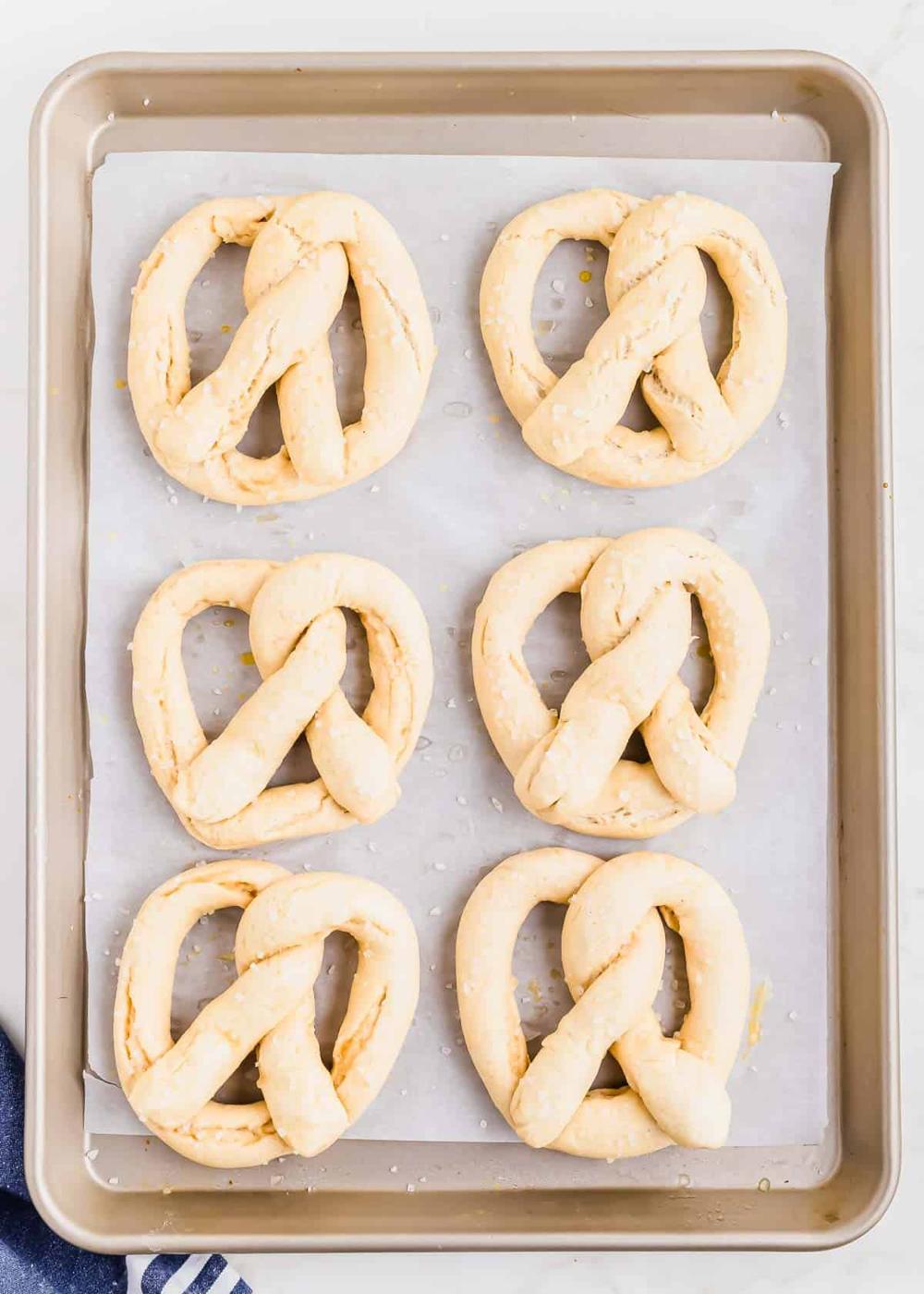 A baking tray with six unbaked gluten-free pretzels arranged in two rows of three, lined with parchment paper, ready to be baked.
