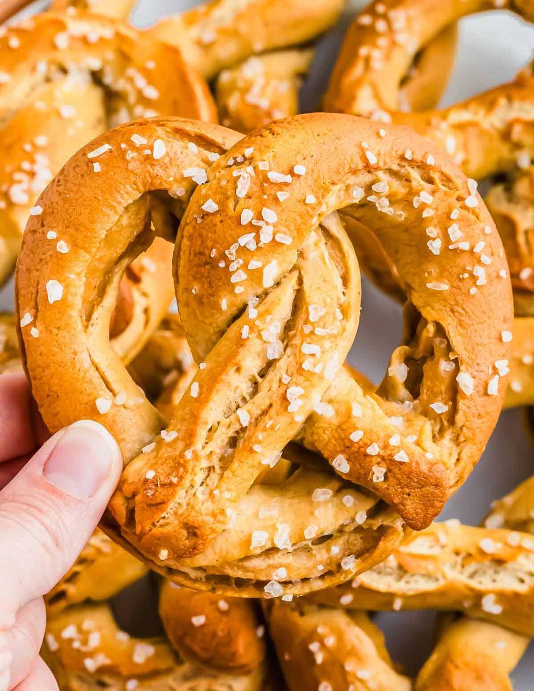 A hand holding a salted gluten free pretzel with several other pretzels in the background.