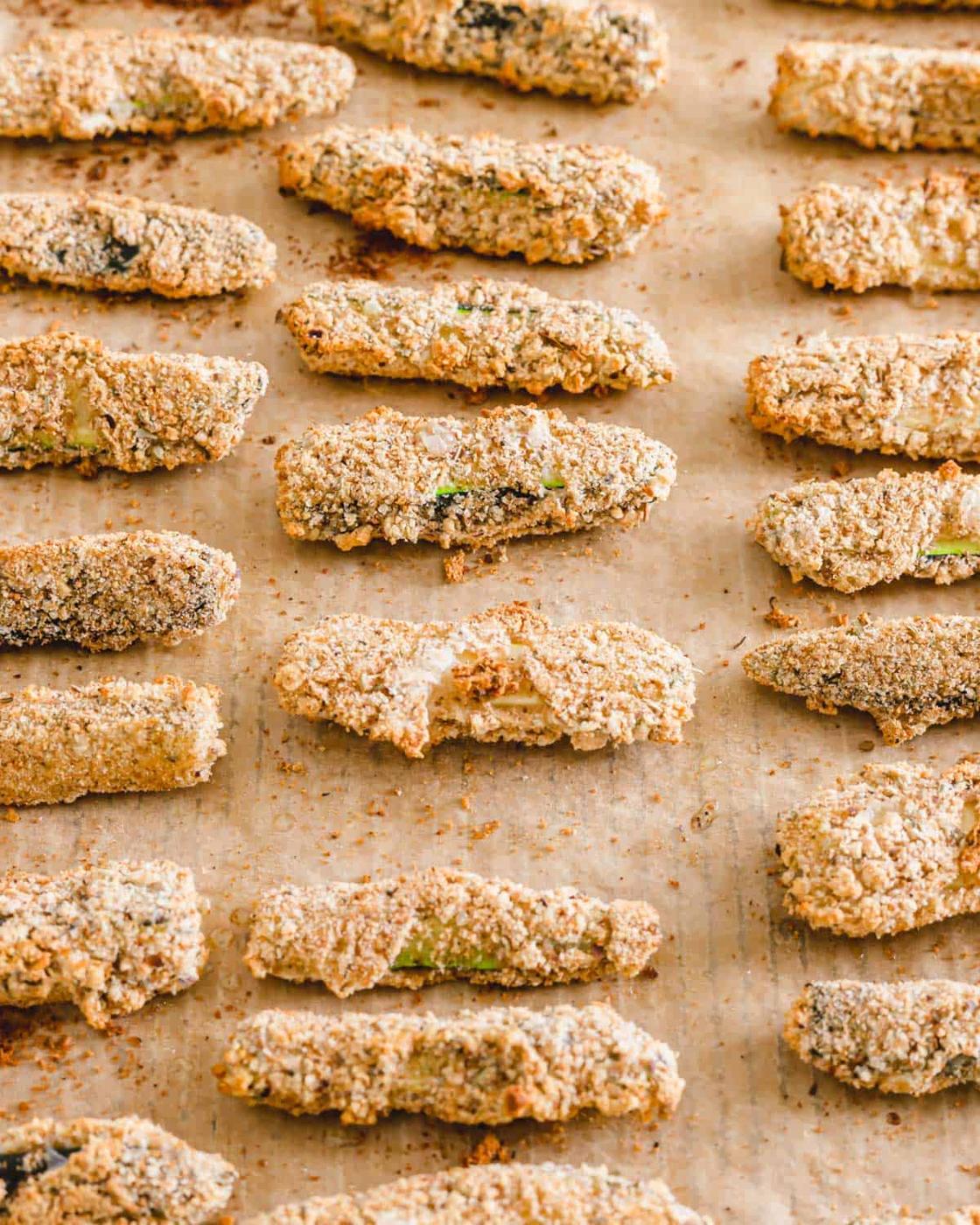 Baked gluten-free and vegan zucchini fries on a parchment lined baking sheet.
