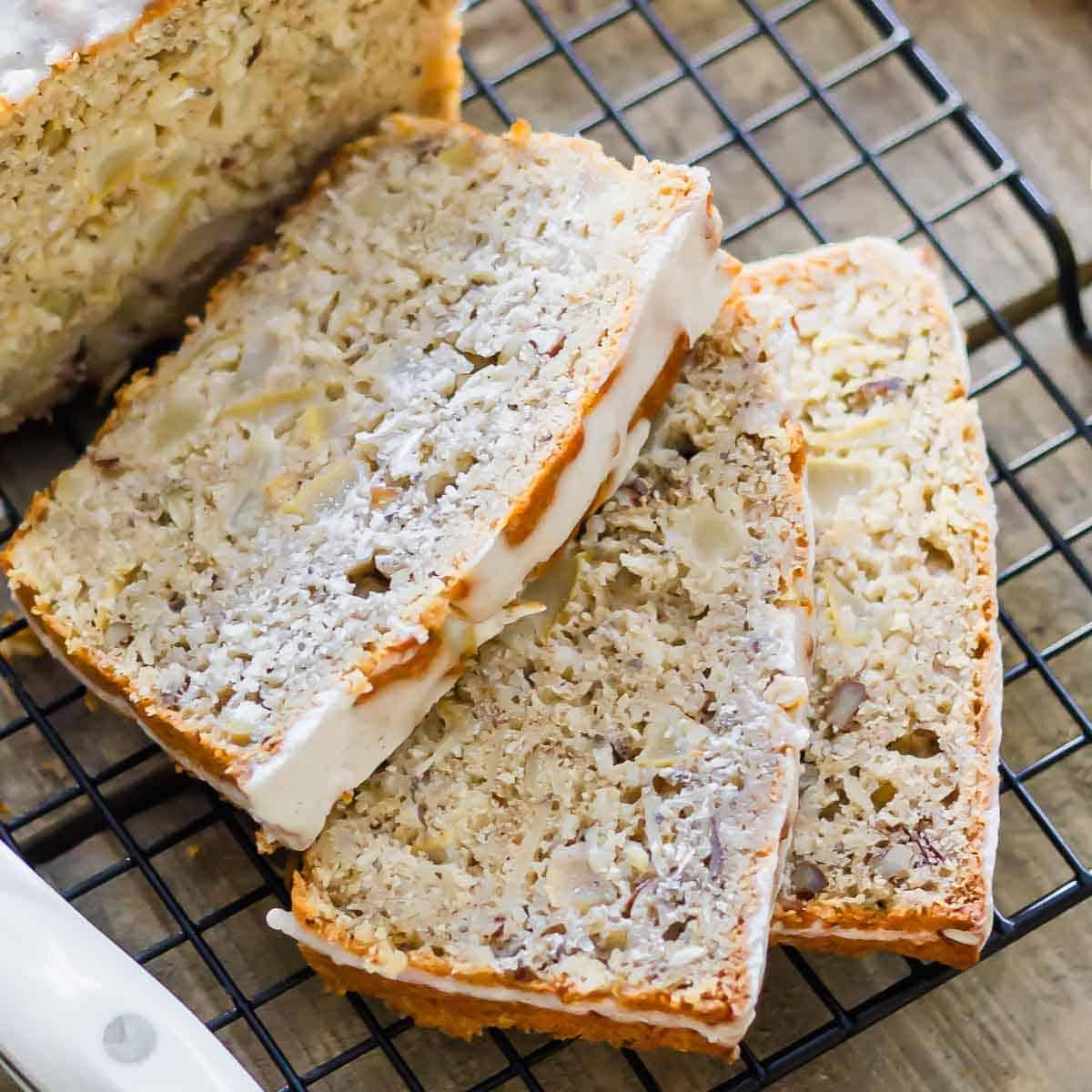 Three slices of a quick bread recipe with visible chunks of pear and moist texture are placed on a cooling rack. One end of the loaf is partially visible on the left side of the image.