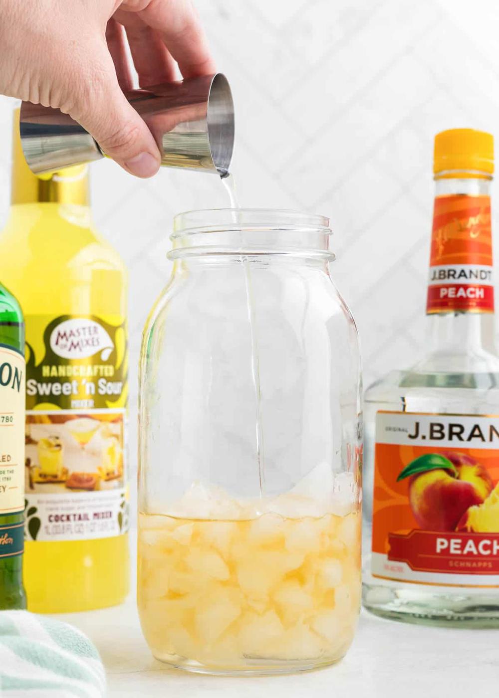 Person pouring liquid from shot glass into mason jar.