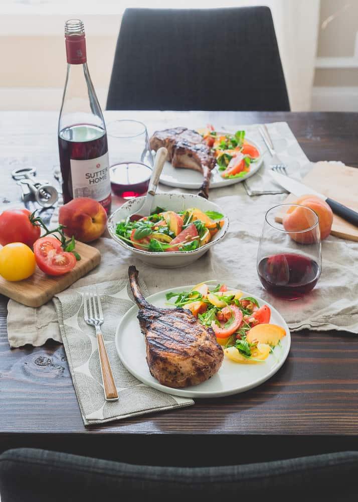 Harissa rubbed grilled pork chops are a simple, spicy summer meal perfectly paired with a ripe peach and tomato salad and glass of sweet red wine.