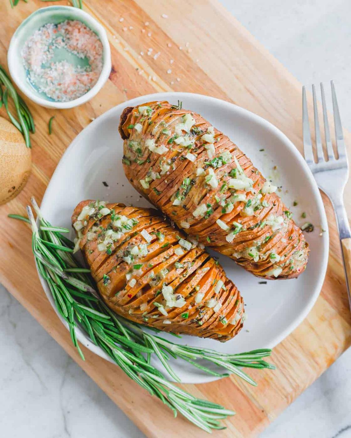 Baked hasselback sweet potatoes on a small plate with rosemary dressing.