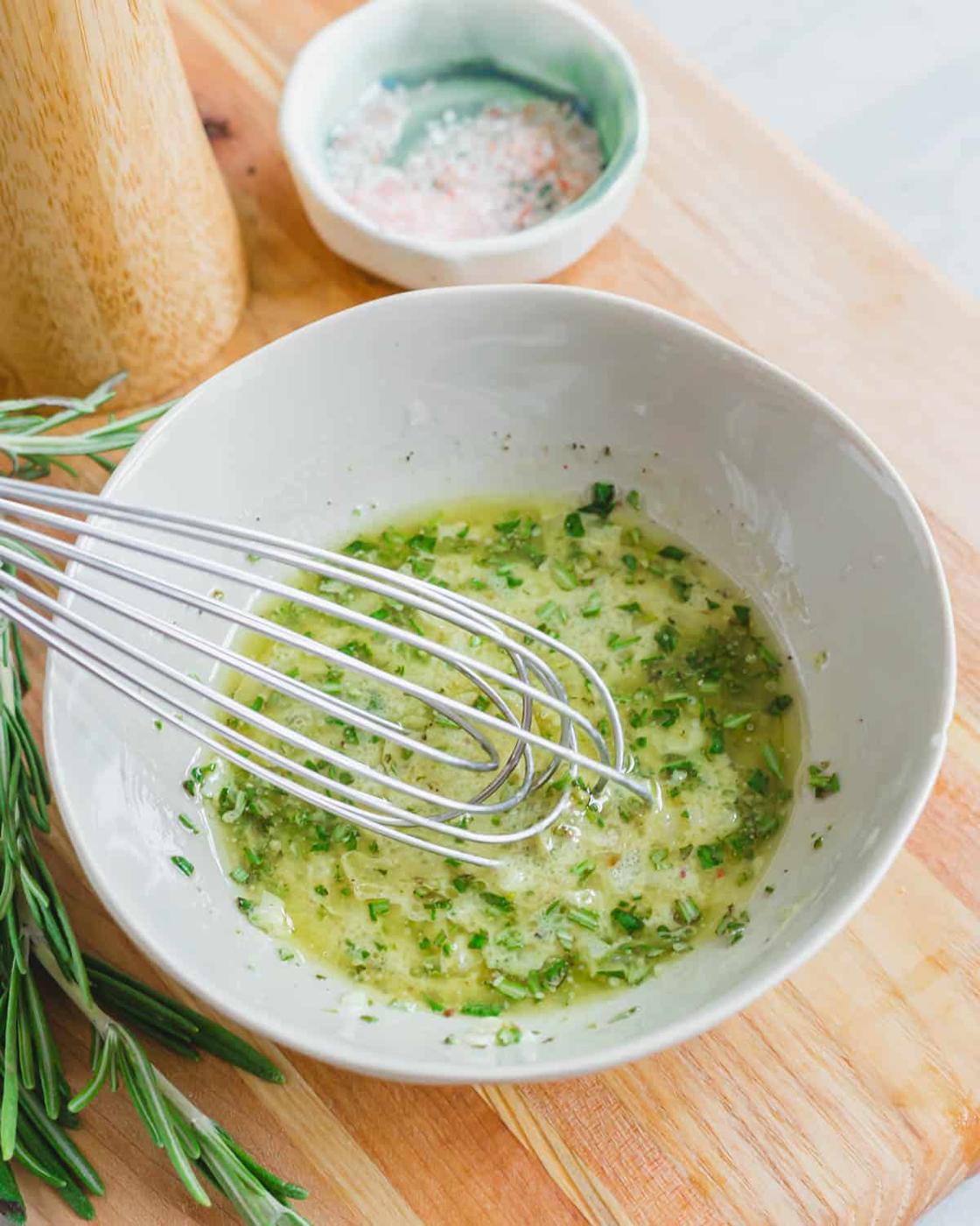 A rosemary mustard vinaigrette dressing in a small bowl with a whisk.