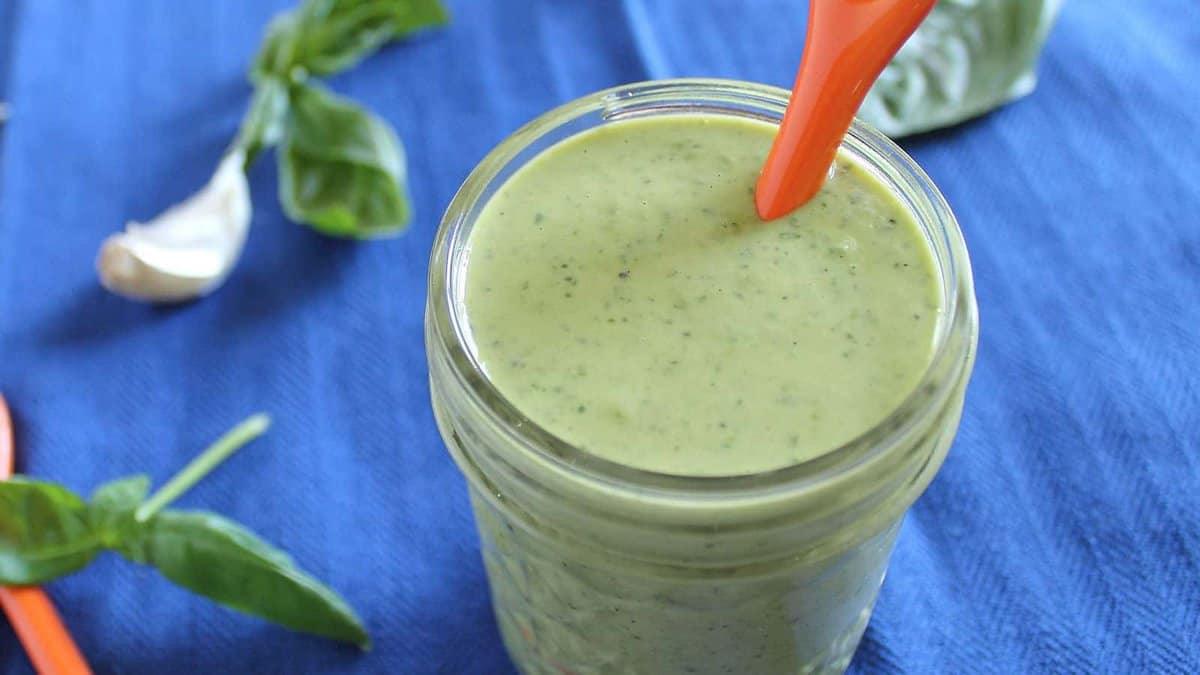 Garlic herb tahini dressing in a jar with basil leaves.