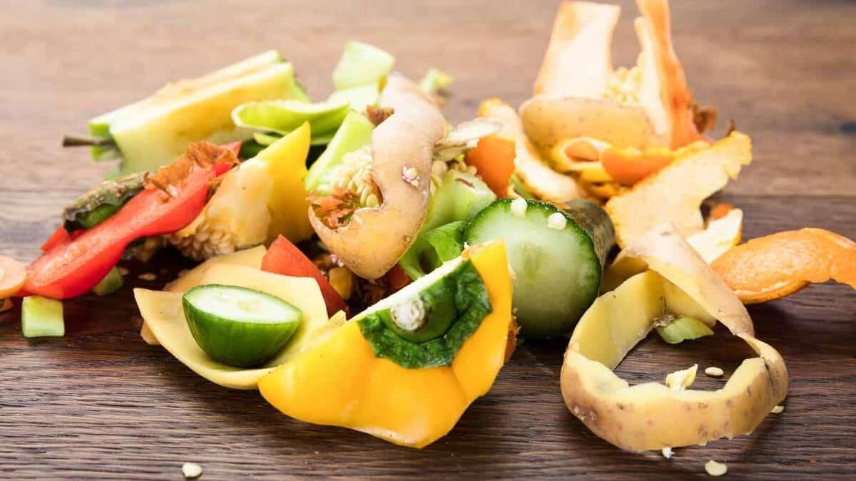 A variety of vegetable peels and scraps, including cucumbers, carrots, and peppers, scattered on a wooden surface.