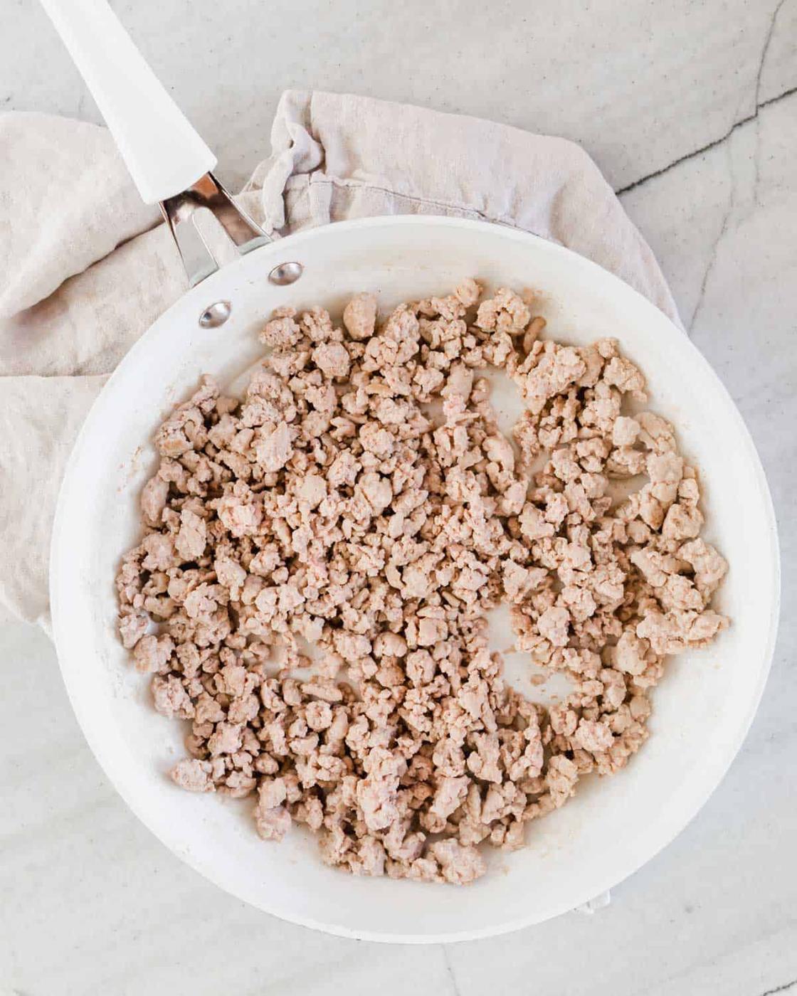 Browned ground turkey meat in a white skillet on top of a kitchen towel.
