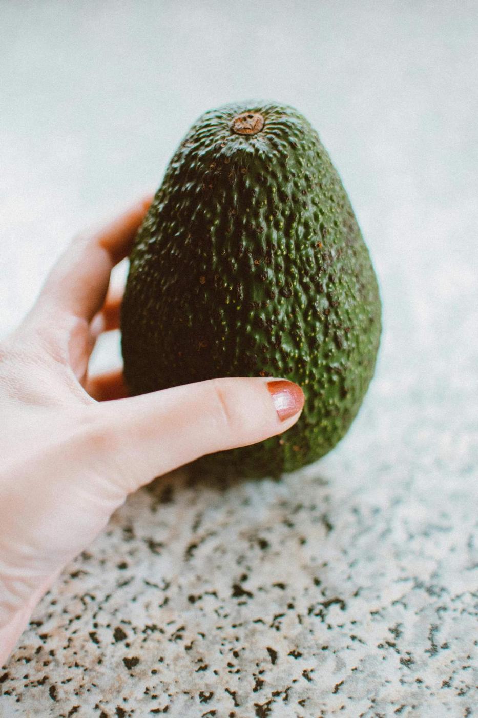 A person holding a ripe Hass avocado against a speckled countertop.