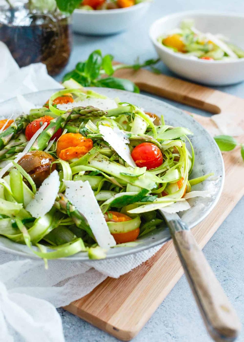 Shaved asparagus salad in a metal plate with a wooden spoon.