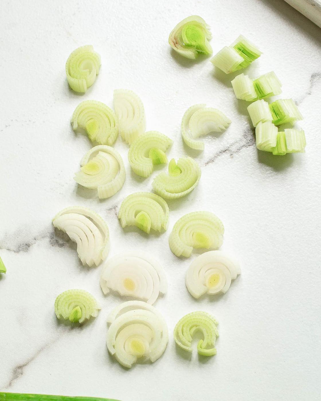 Leeks cut into half circles on a white surface.