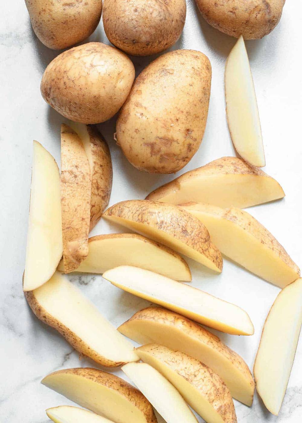 Potatoes and potato wedges on white surface.