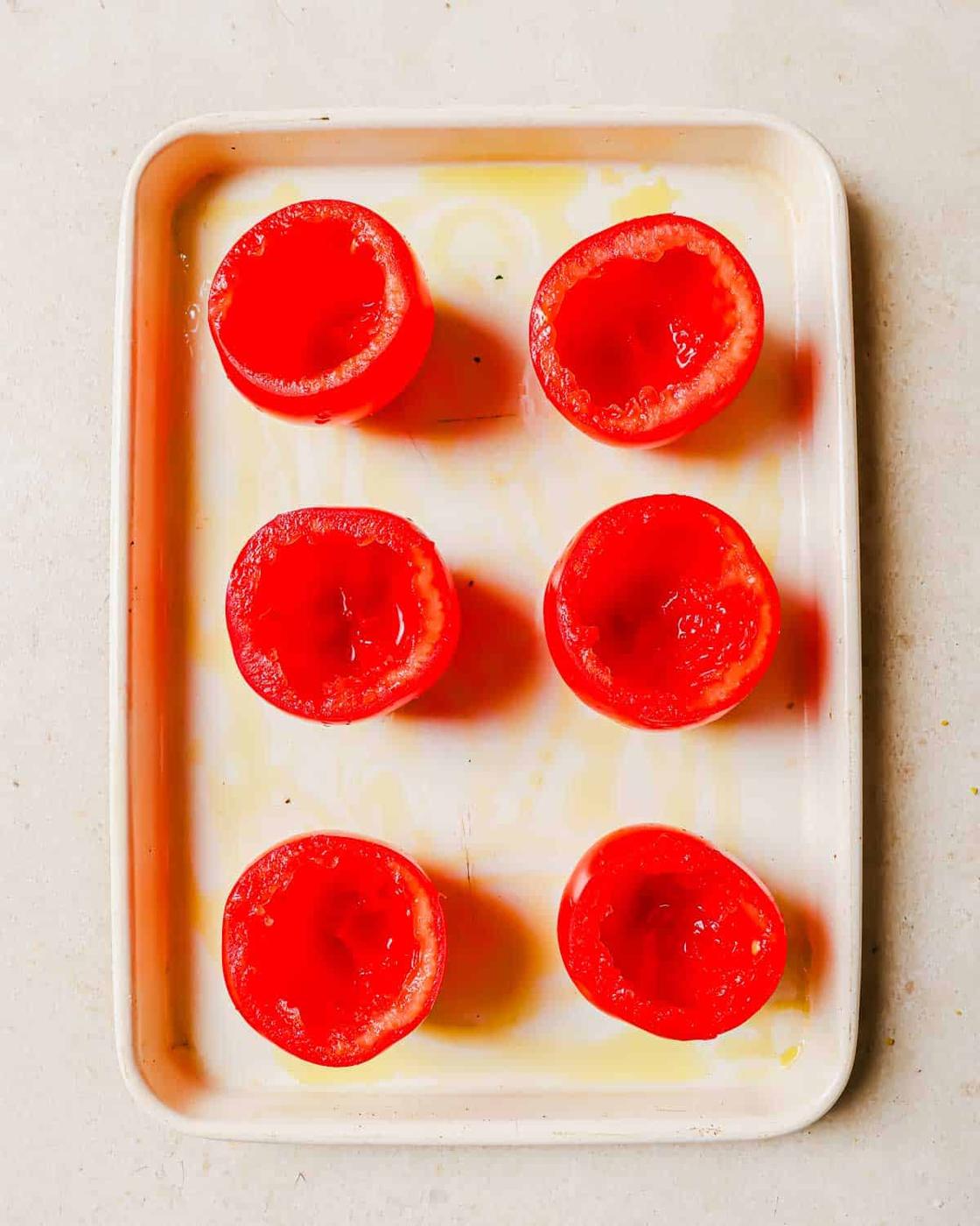 Six hollowed-out ripe tomatoes are placed in two rows on a rectangular white tray.