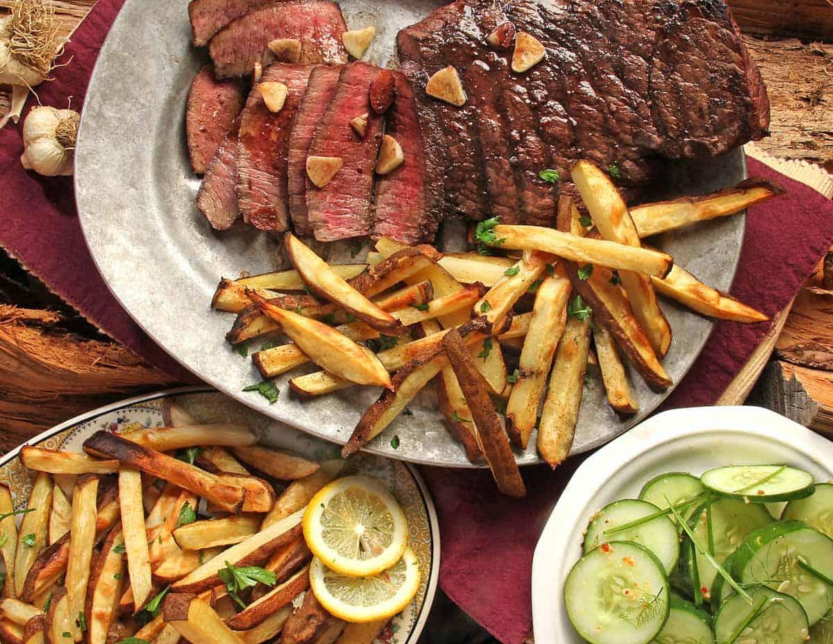Sliced steak with fries and cucumber salad on the side.