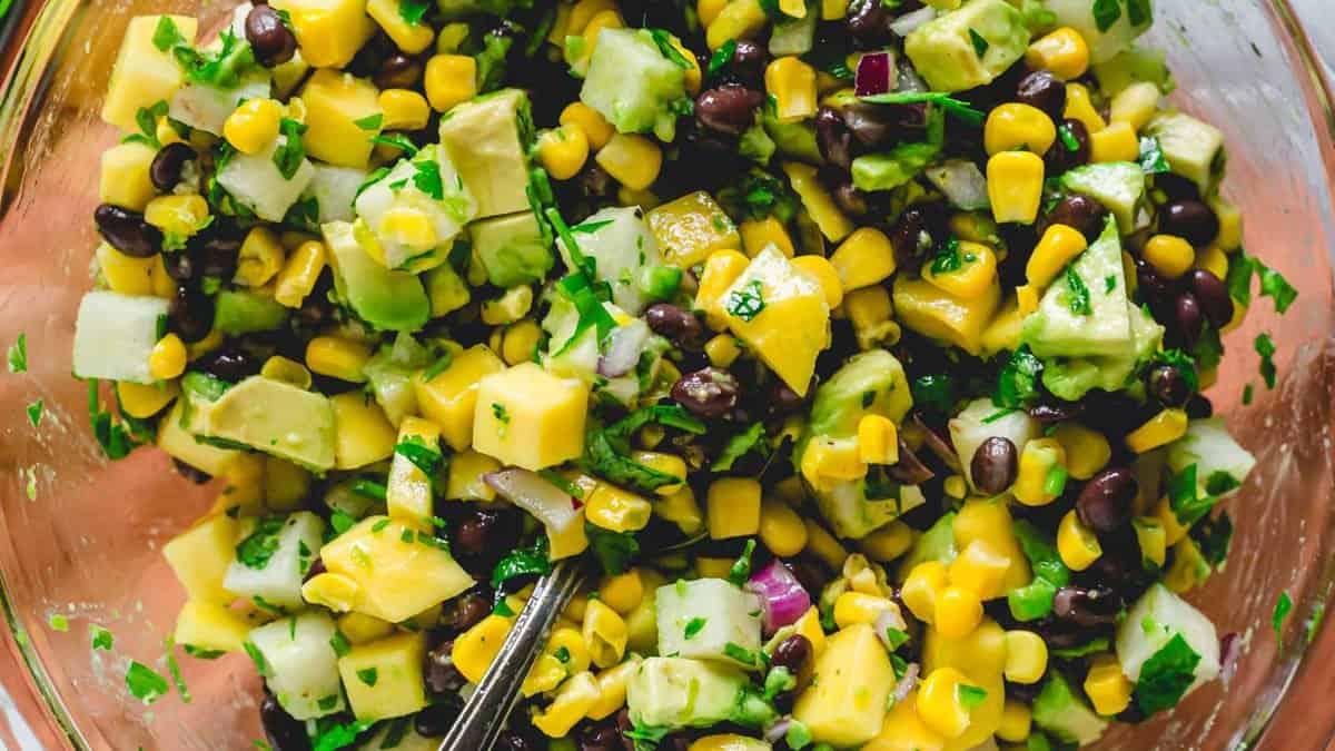 A bowl of mango, black bean and corn salad with a spoon.