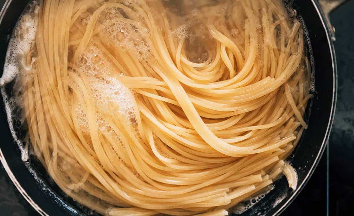A close-up view of uncooked spaghetti noodles boiling in a pot of water, with bubbles forming on the surface.