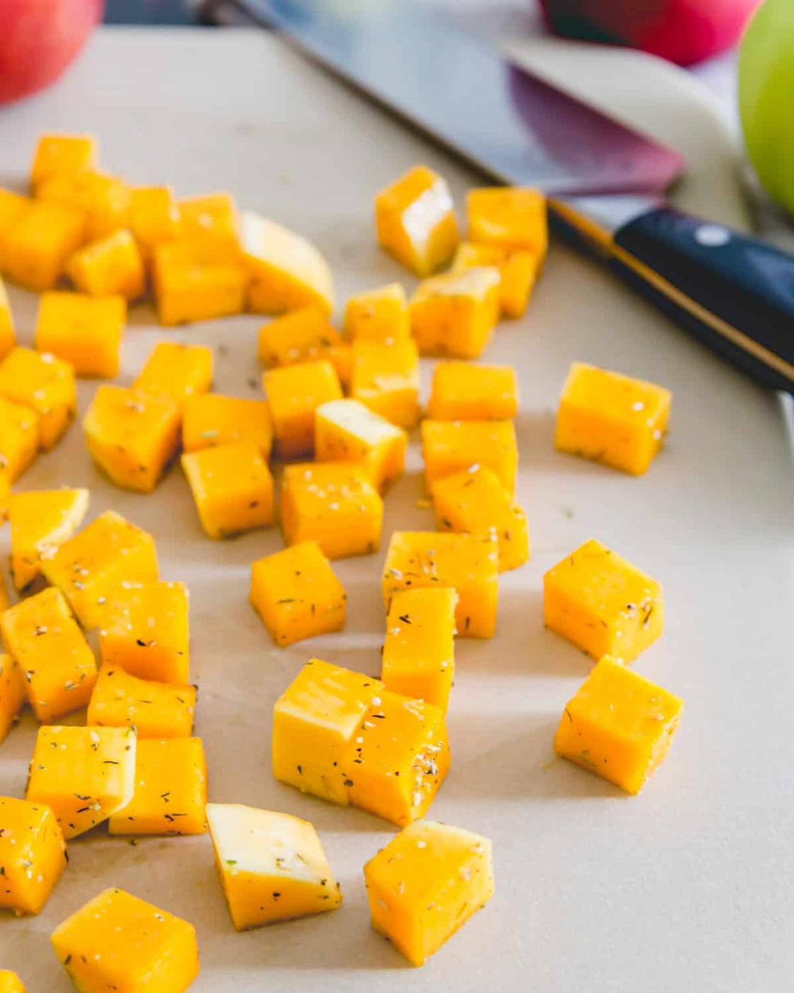 rosemary seasoned butternut squash cubes on a stoneware roasting sheet before baking