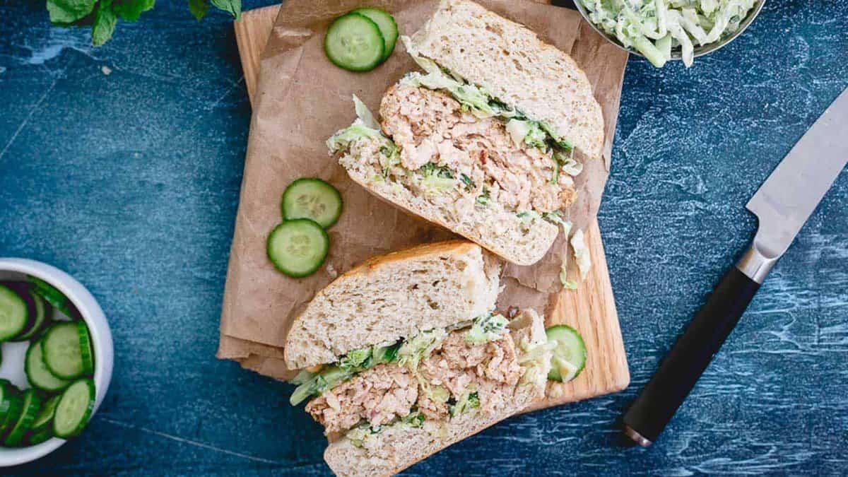 Chicken burgers and cucumbers on a wooden cutting board.