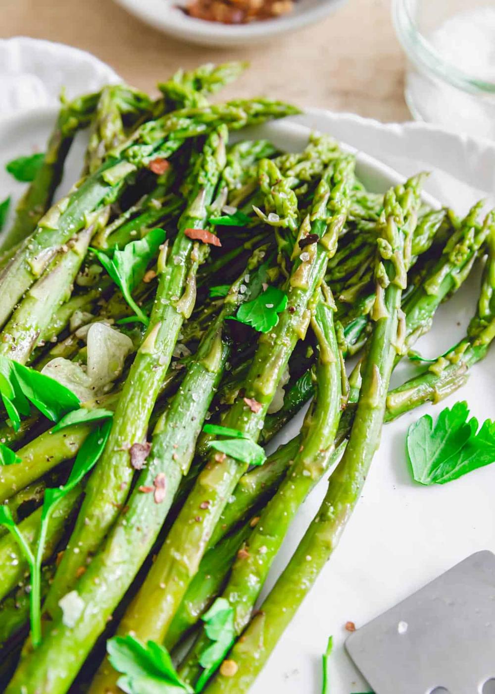 Tender cooked spring asparagus made in the Instant Pot on a plate with sea salt, parsley, garlic and chili flakes.